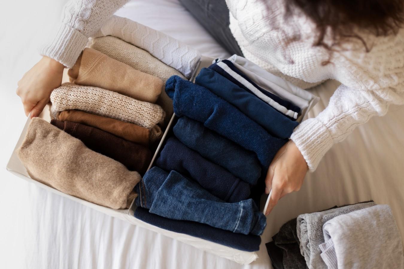 close up hands holding box of clothes: jeans and sweaters